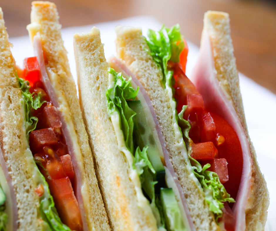 Close-up of fresh ham, lettuce, and tomato sandwiches on white bread.
